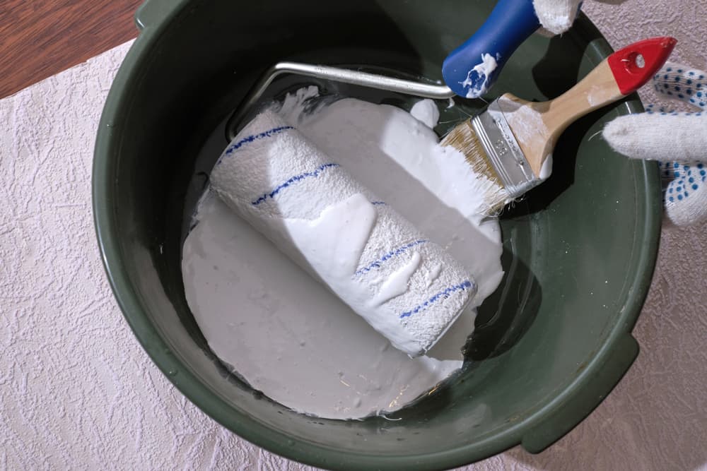 Bucket of white paint with a brush and a roller