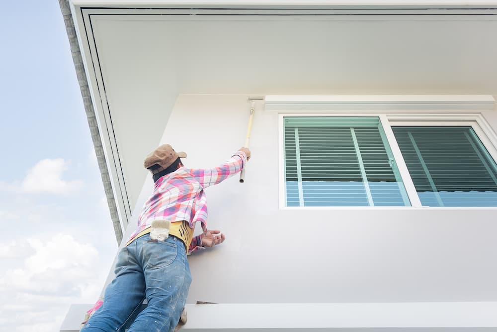 person painting house with long roller brush